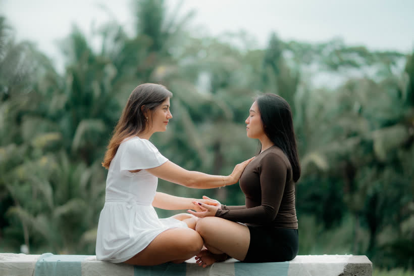 Diana sitting knee to knee with a client, one hand on their chest, both hands held