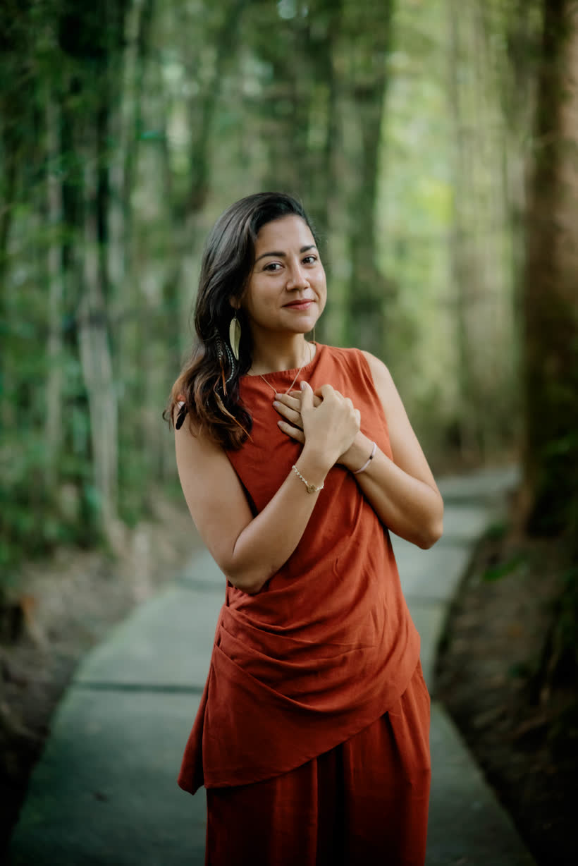 Diana on a forest path, one hand on her heart, looking at the camera